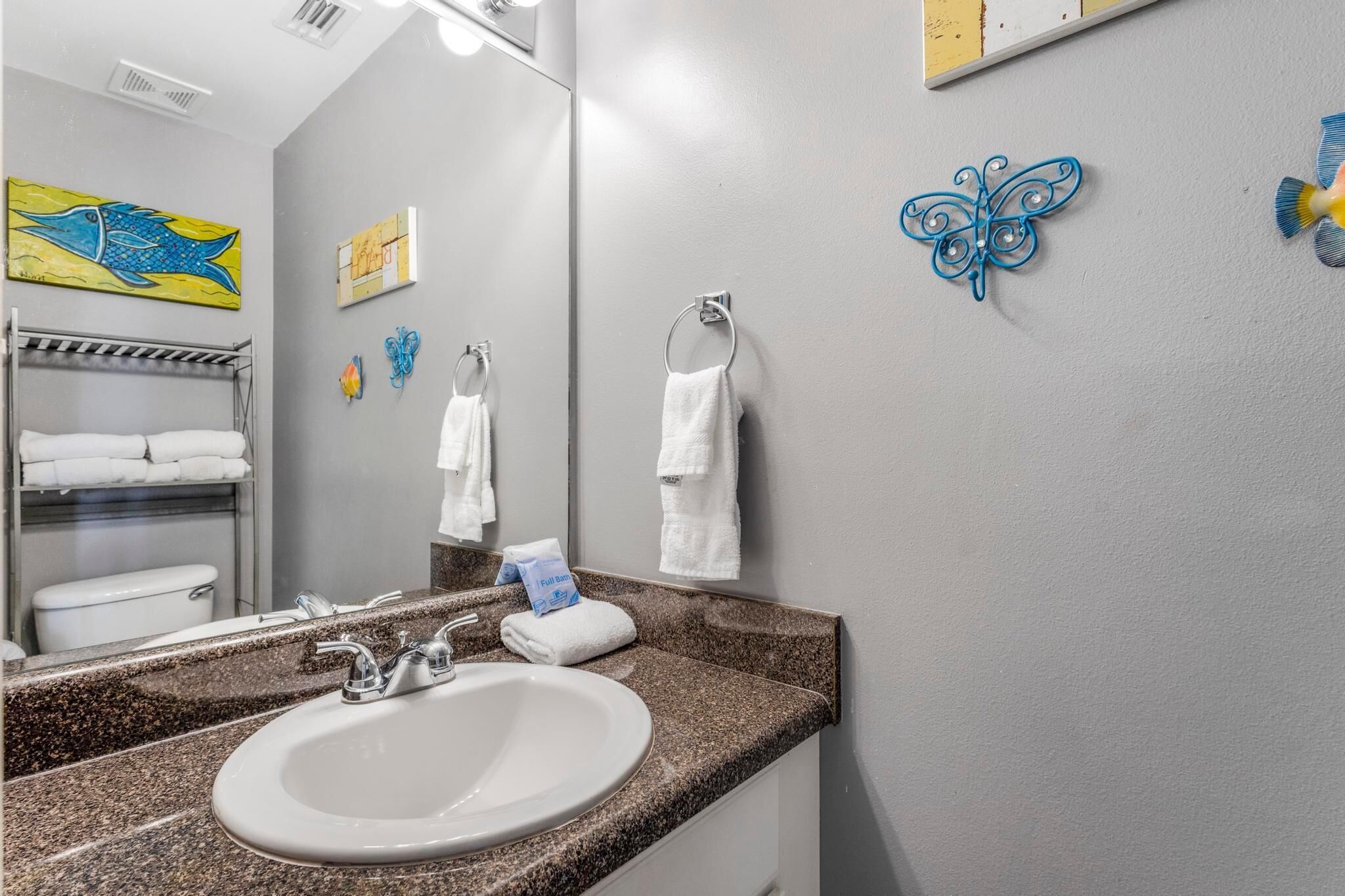 A bathroom with a granite countertop sink, two towel rings, a full bath sign, and a mirror.