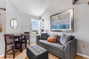 A living room with a grey sofa, a dining table with chairs, a window with shutters, and a framed picture on the wall. - Grand Caribbean 423 (Orange Beach)