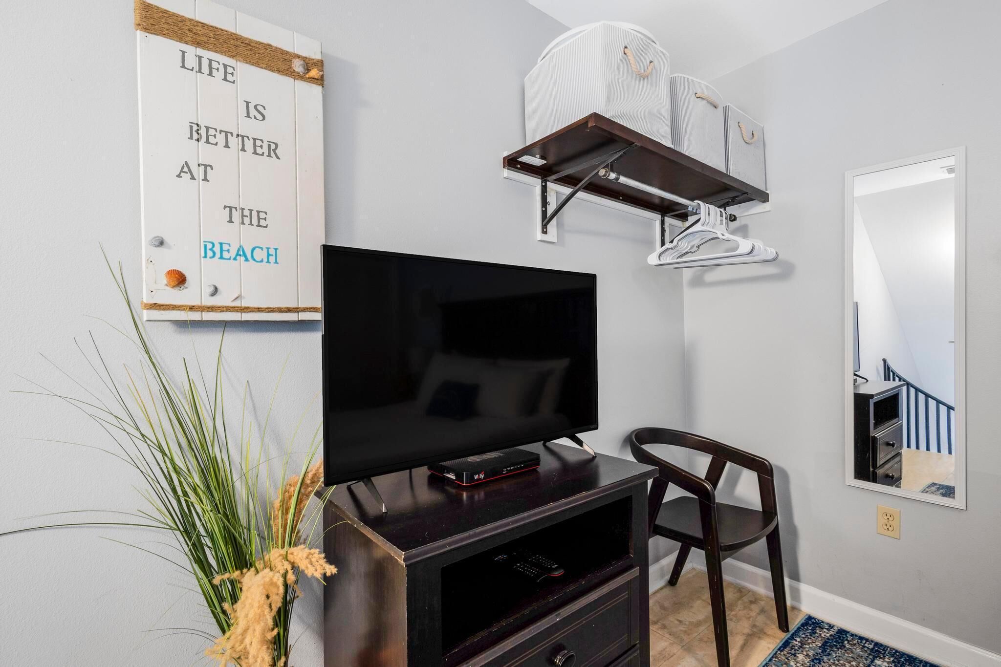 A room with a flat-screen TV on a wooden stand, a chair, a wall-mounted fan, and a motivational quote sign.