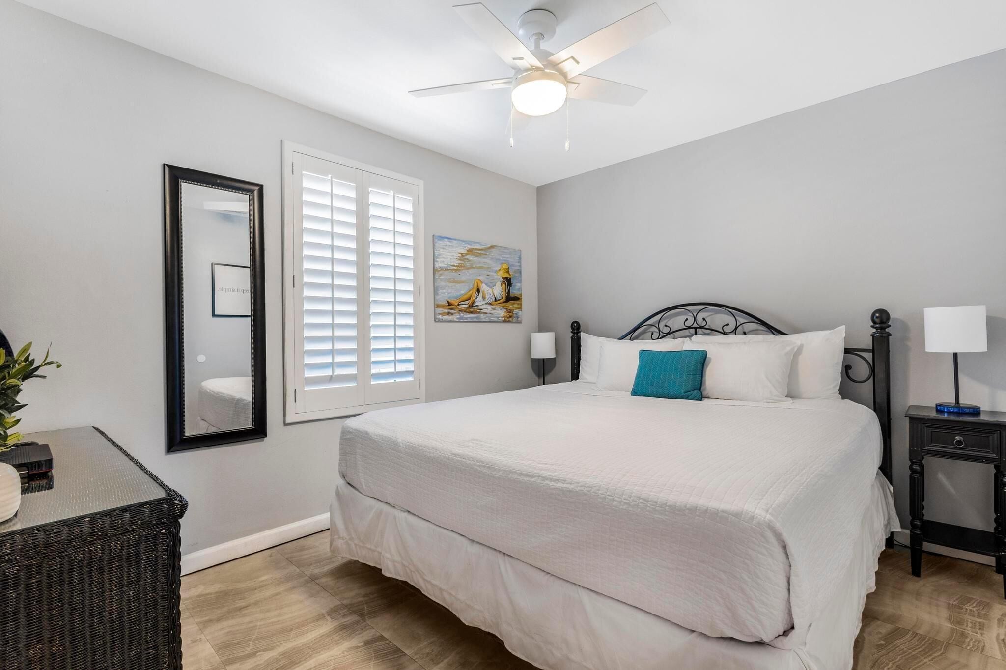A bedroom with a bed, a ceiling fan, a window with blinds, and a painting on the wall.