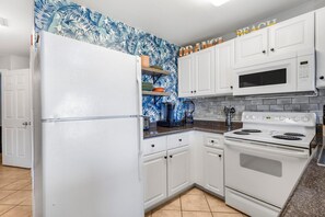 Una cocina con armarios blancos, un refrigerador, un microondas y una estufa.