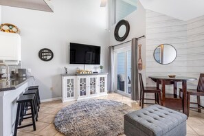 A modern kitchen with a flat-screen TV, a dining area with a round table and chairs, and a cozy seating area with an ottoman. - Grand Caribbean 423 (Orange Beach)