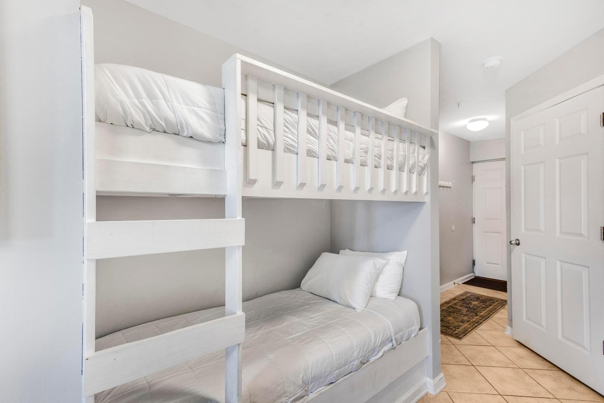 A bunk bed room with a door and a rug on the floor.