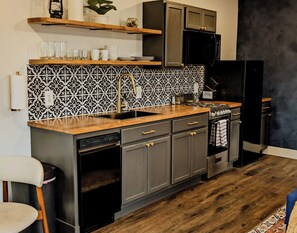 A kitchen with a patterned backsplash, dark cabinets, a black refrigerator, and a wooden countertop. - Indigo Studio - Poolside, Near Fort & Birding (Sierra Vista)