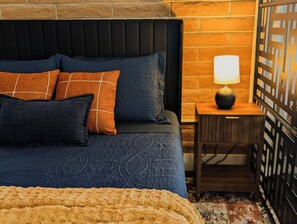 Ein Bett mit dunklem Kopfteil, mehreren Kissen, einer flauschigen Decke und einem Nachttisch mit Lampe.
