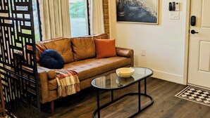 Uma sala de estar com um sofá marrom, uma mesa de centro de vidro e um quadro na parede.