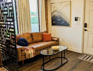 Ein Wohnzimmer mit einem braunen Sofa, einem Glastisch und einem Bild an der Wand.