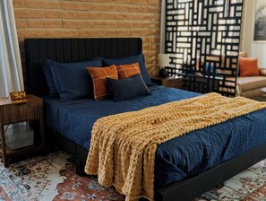 A bed with a dark headboard, multiple pillows, a knitted throw, and a wooden nightstand with a clock. - Indigo Studio - Poolside, Near Fort & Birding (Sierra Vista)