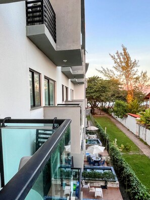 Edifici modern amb un balcó de vidre que ofereix vista a un jardí paisatjistic amb mobiliari d'exterior.