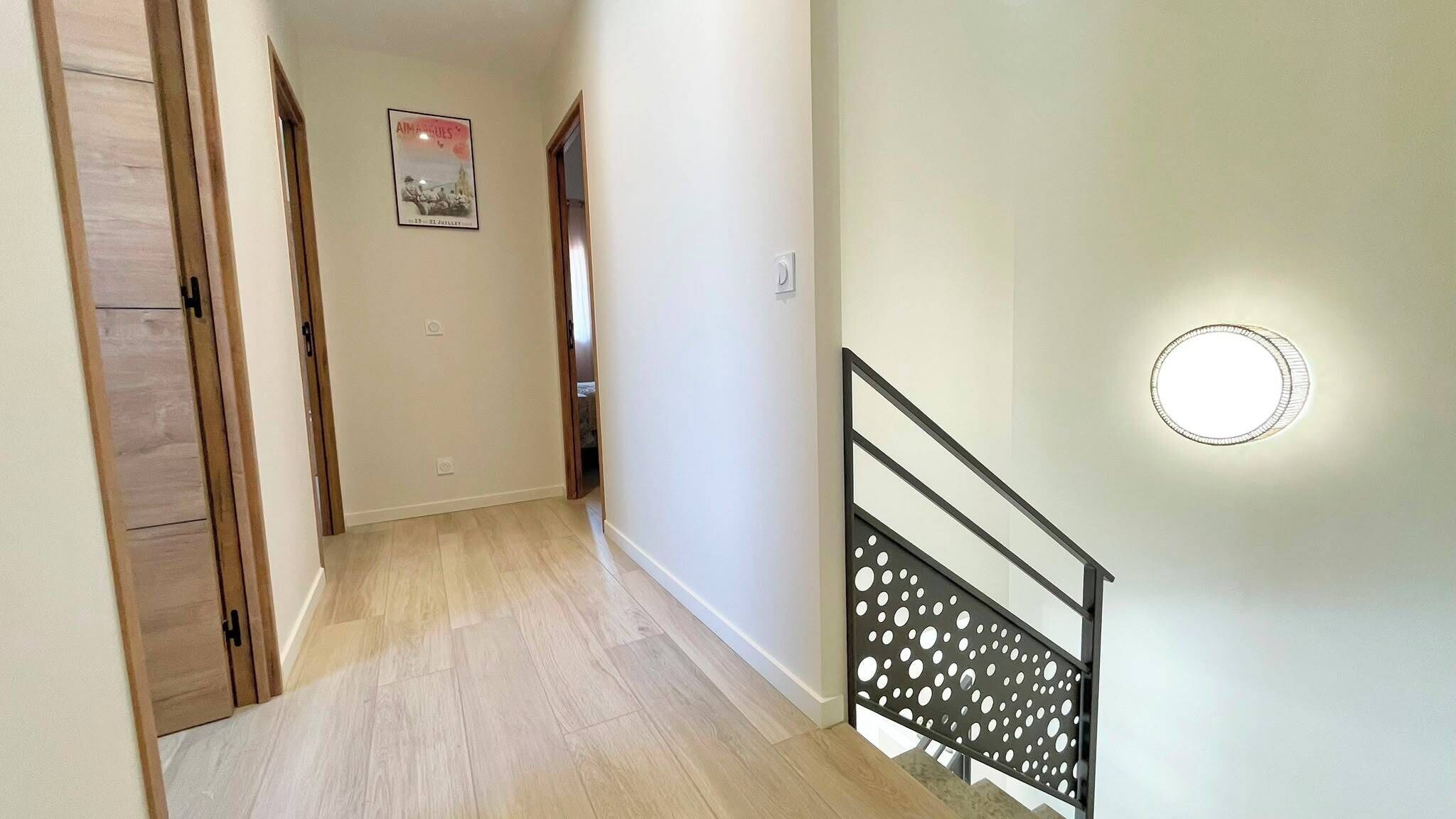 Un couloir avec une porte en bois, une affiche accrochée au mur et un escalier doté d’une rampe en métal.
