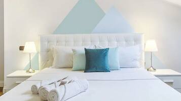 Un lit bien fait, avec des oreillers blancs et turquoise, deux lampes de chevet et une serviette pliée posée sur le lit.