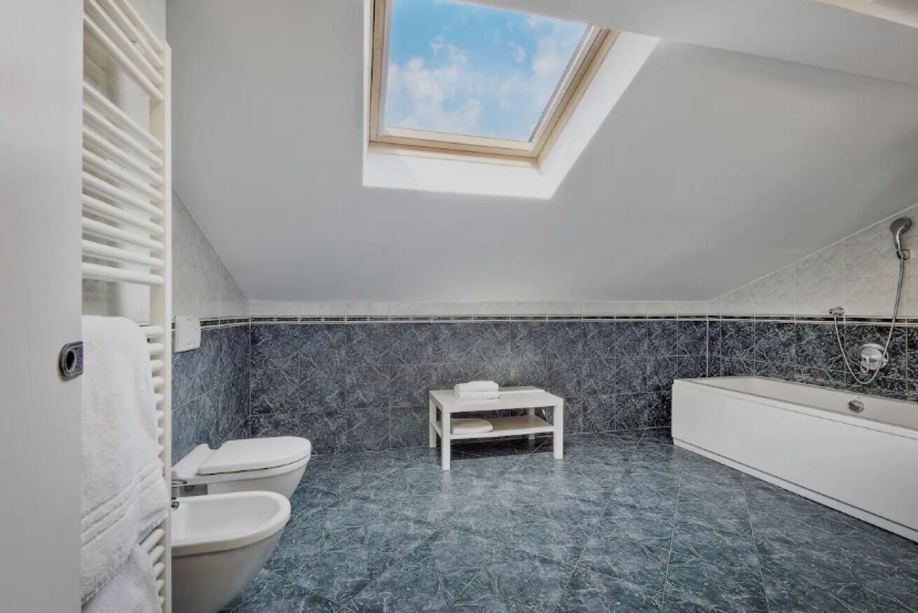 Une salle de bain moderne avec un puits de lumière, des toilettes, une baignoire et une petite table sur laquelle est posée une serviette.