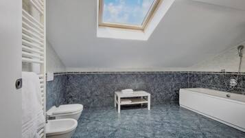 Une salle de bain moderne avec un puits de lumière, des toilettes, une baignoire et une petite table sur laquelle est posée une serviette.