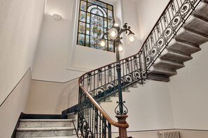 Eine Treppe mit aufwendiger Metallgeländerung und einem Holnlauf, der zu einem Raum mit einem großen Buntglasfenster führt.