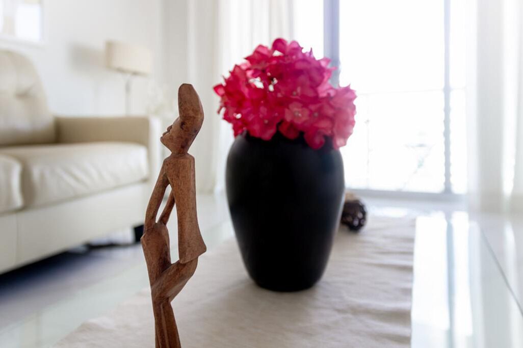 En skulptur på ett bord, en vas med rosa blommor och en vit soffa i ett väl upplyst rum.
