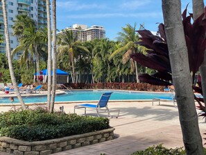 A pool area with lounge chairs, palm trees, and a building in the background. - Beauty apt Sunny Isles, 16th Floor. Great views! (Sunny Isles Beach)