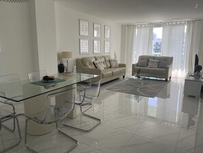 A modern living room with a glass dining table, two sofas, and a large window with curtains. - Beauty apt Sunny Isles, 16th Floor. Great views! (Sunny Isles Beach)