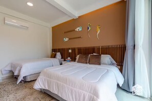 Quarto de hotel com duas camas, uma cabeceira de madeira, ar-condicionado fixado na parede e uma janela com cortinas.