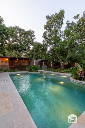 A swimming pool surrounded by lush greenery and a building with outdoor lighting. - Luxury TopSpot Villa Para 16 a 150 mts de la Playa (Santa Marta)