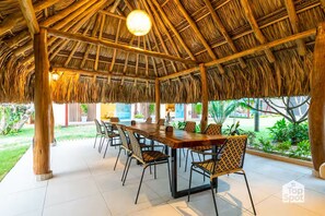 A covered outdoor dining area with a thatched roof, a long wooden table, and wicker chairs. - Luxury TopSpot Villa Para 16 a 150 mts de la Playa (Santa Marta)