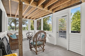 A covered patio with wooden beams, white walls, and large windows offering views of trees and a body of water. - Solara on the Lake (Plymouth)