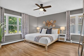 A bedroom with a bed, two bedside tables, a ceiling fan, and a window with curtains. - Solara on the Lake (Plymouth)