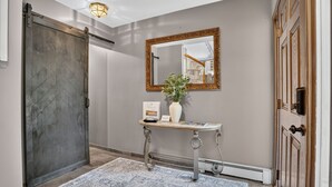 A hallway with a sliding door, a console table with a vase and a framed item, a mirror on the wall, and a patterned rug. - Solara on the Lake (Plymouth)