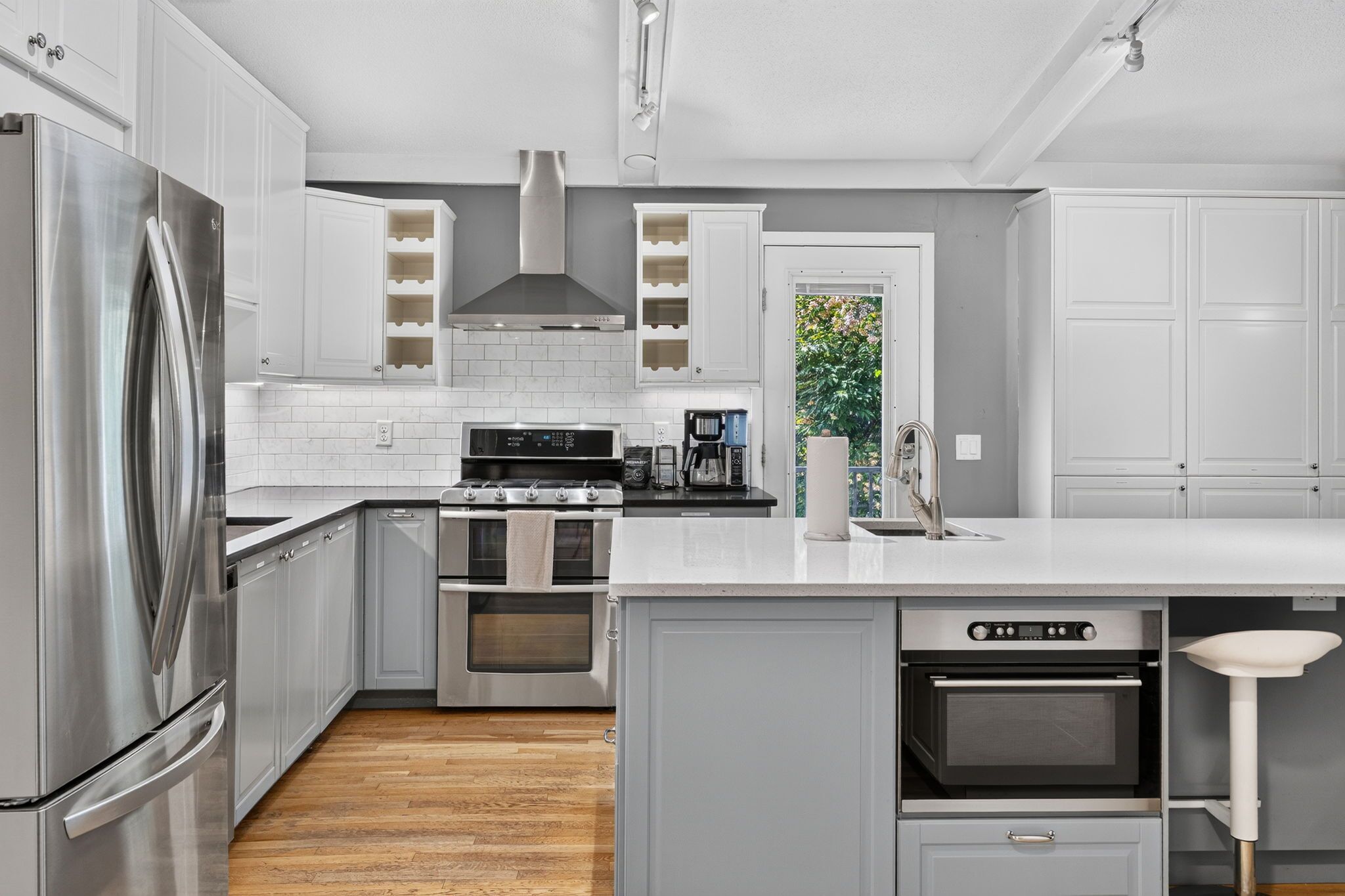 A modern kitchen with stainless steel appliances, white cabinetry, and a wooden floor.