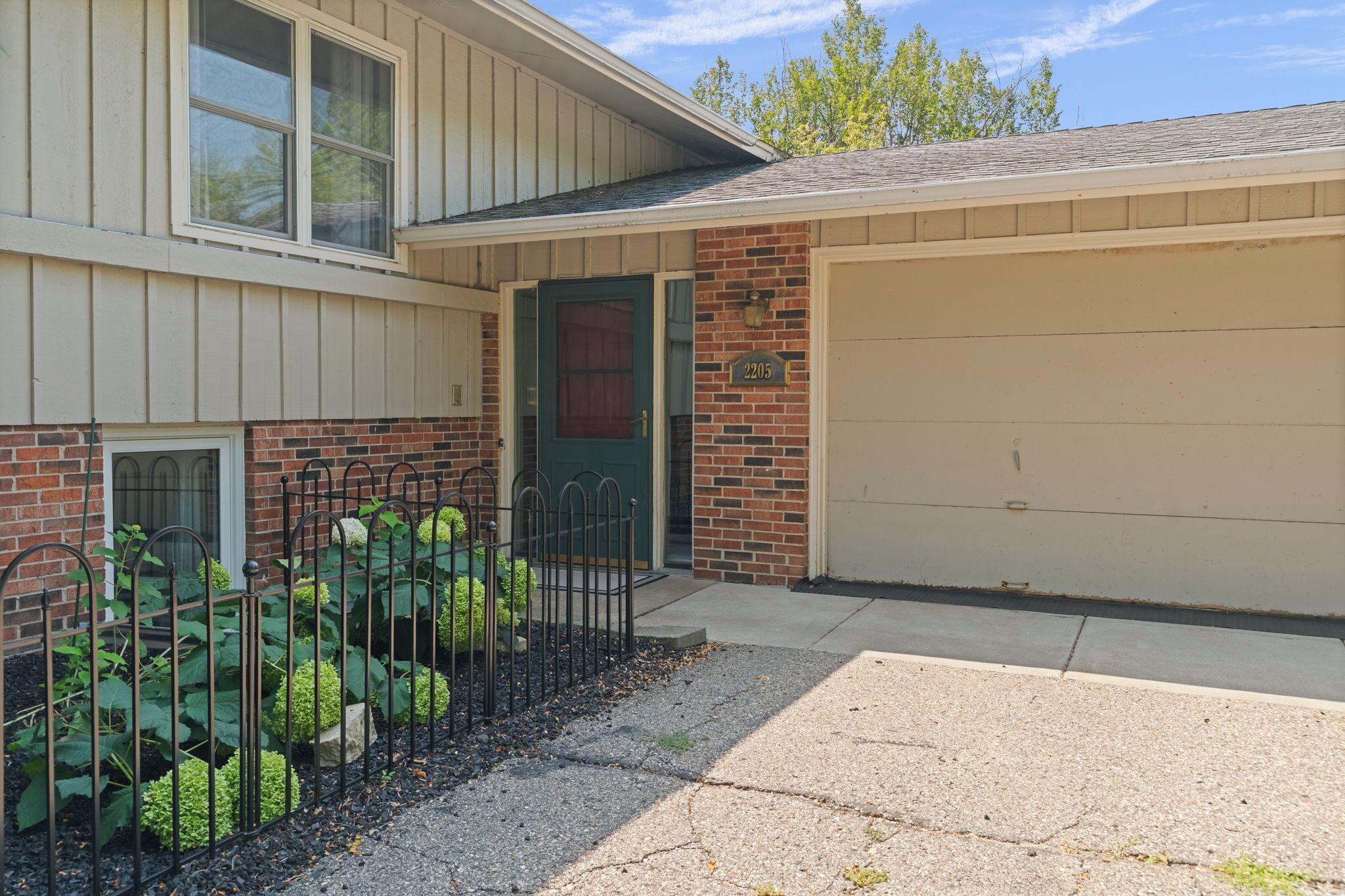 A residential house with a garage, a front door, and a small garden area with a metal fence.