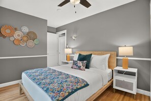 A modern bedroom with a bed, bedside tables, a ceiling fan, and decorative wall art. - Solara on the Lake (Plymouth)