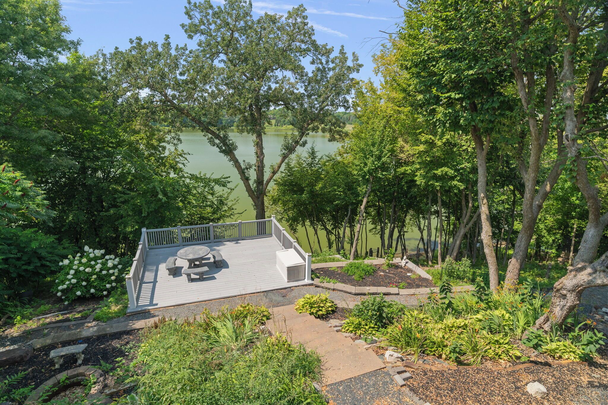 Een terras met een tafel en banken met uitzicht op een meer, omringd door bomen en begroeiing.