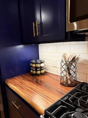 A kitchen with dark blue cabinets, a wooden countertop, a gas stove, a spice rack, and a utensil holder.