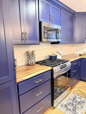 A kitchen with dark blue cabinets, a stainless steel microwave, a gas stove, and a built-in oven.