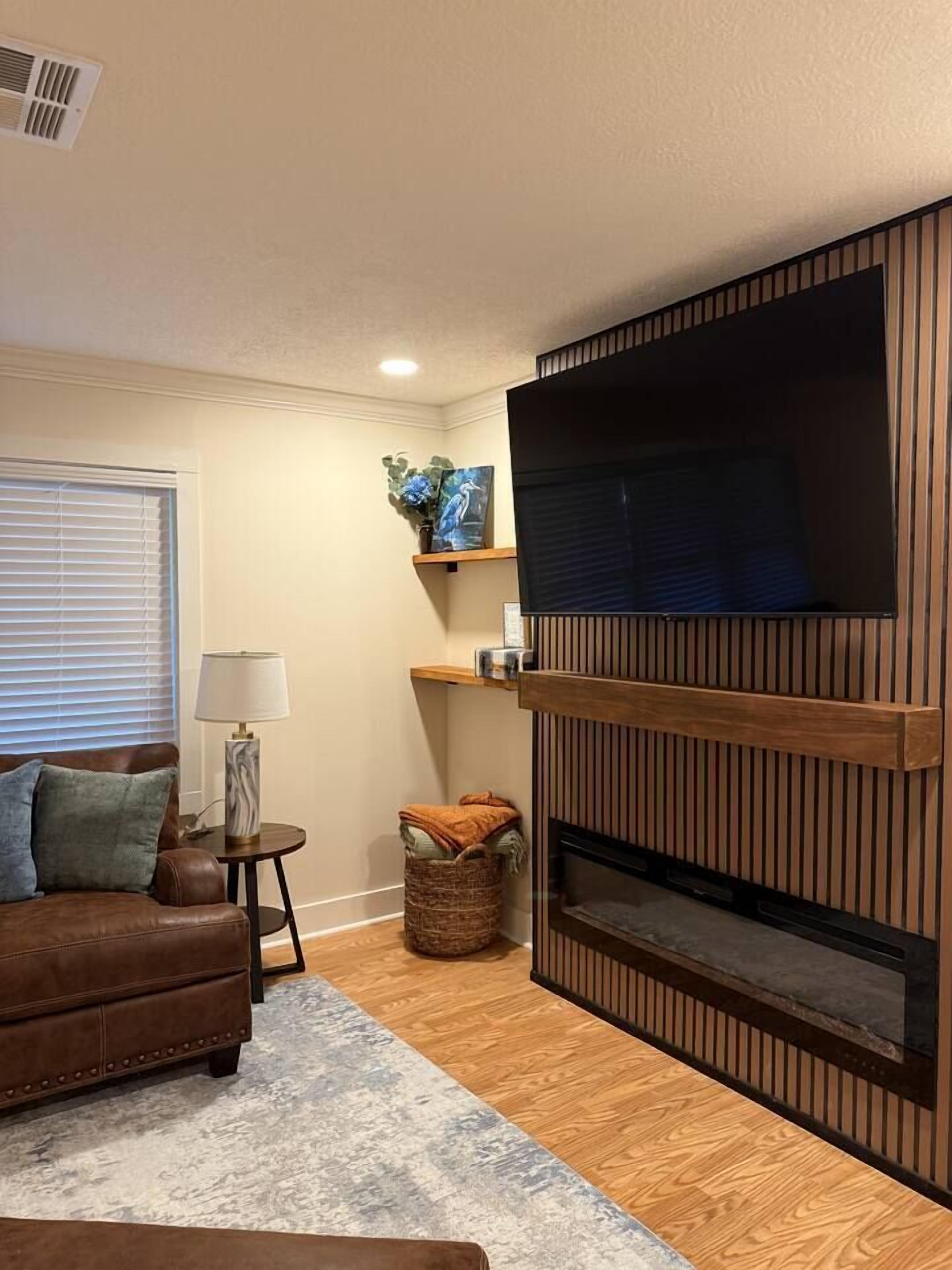 A living room with a brown leather sofa, a side table with a lamp, a wooden TV stand, and a fireplace.
