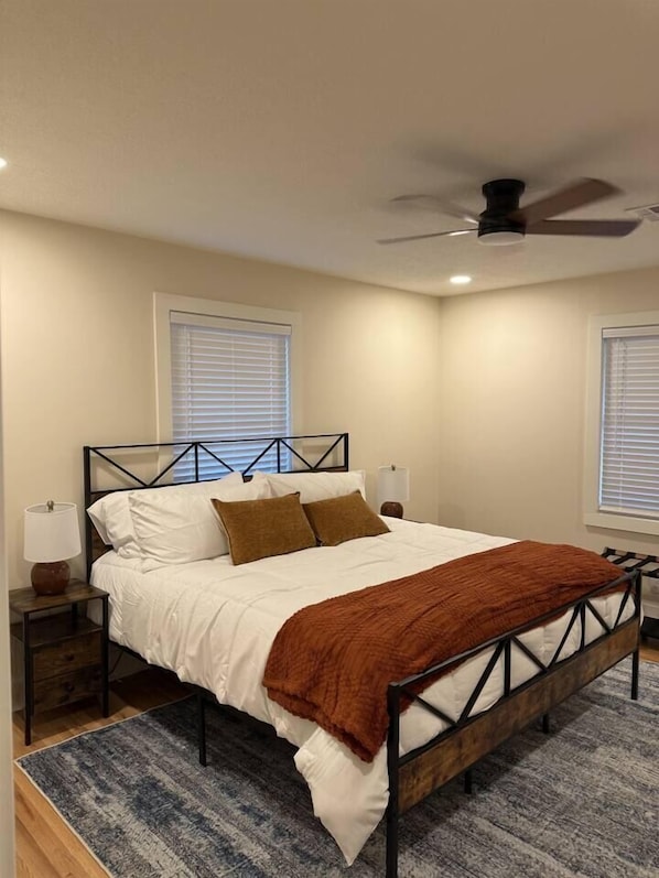 A bedroom with a bed, nightstands, a ceiling fan, and two windows with blinds.
