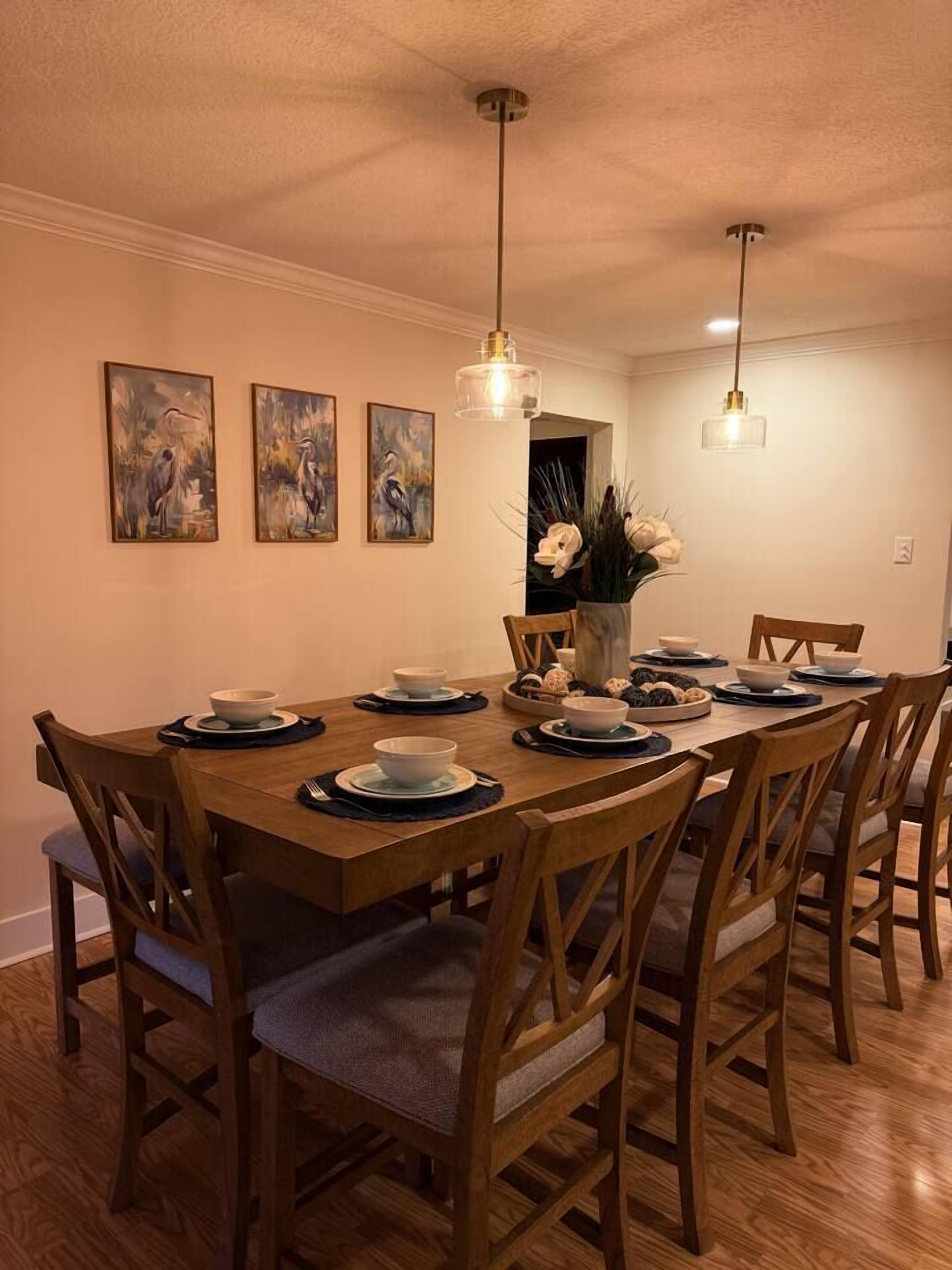 Una sala da pranzo con un tavolo in legno apparecchiato per quattro persone, circondato da sedie, opere d'arte a parete e illuminazione a sospensione.