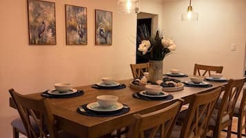 Una sala da pranzo con un tavolo in legno apparecchiato per quattro persone, circondato da sedie, opere d'arte a parete e illuminazione a sospensione.