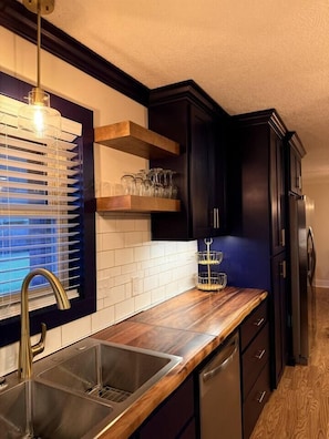 A modern kitchen with dark cabinetry, a wooden countertop, a stainless steel sink, and a built-in wine rack.