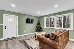 A living room with a brown couch, a wooden coffee table, a Christmas tree, and a large window with blinds.