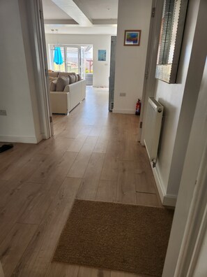 Un passadís amb terra de fusta que condueix a una zona d'estar amb un sofà blanc i un radiador.
