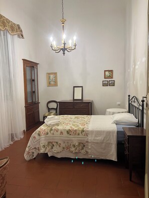 A bedroom with a bed, a dresser, a chair, a desk, a chandelier, and a cabinet.