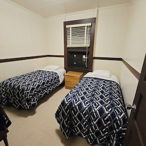 Una habitación con dos camas, una ventana con persianas, una mesita de noche de madera y una puerta.
