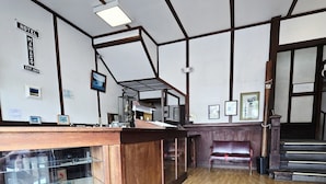 A hotel reception area with a wooden counter, framed pictures on the walls, and a staircase leading to an upper level. - Manago Hotel (Captain Cook)