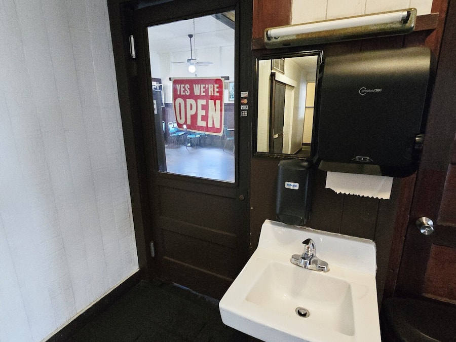 A bathroom with a white sink, a mirror, and a door with a 'YES WE'RE OPEN' sign.