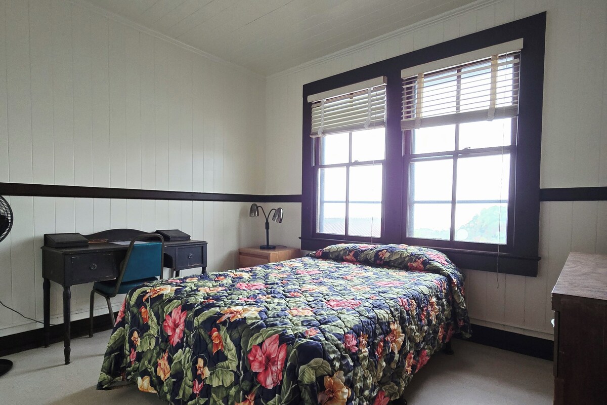 A bedroom with a bed, a desk, a chair, a lamp, and a window with blinds.