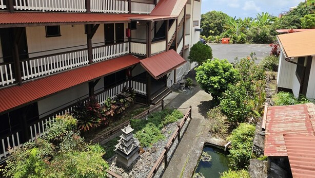 A multi-story building with balconies, a courtyard with a water feature, and surrounding greenery. - Manago Hotel (Captain Cook)
