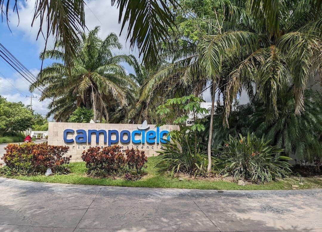 A sign for 'Camposoles' with palm trees and shrubs in the foreground.