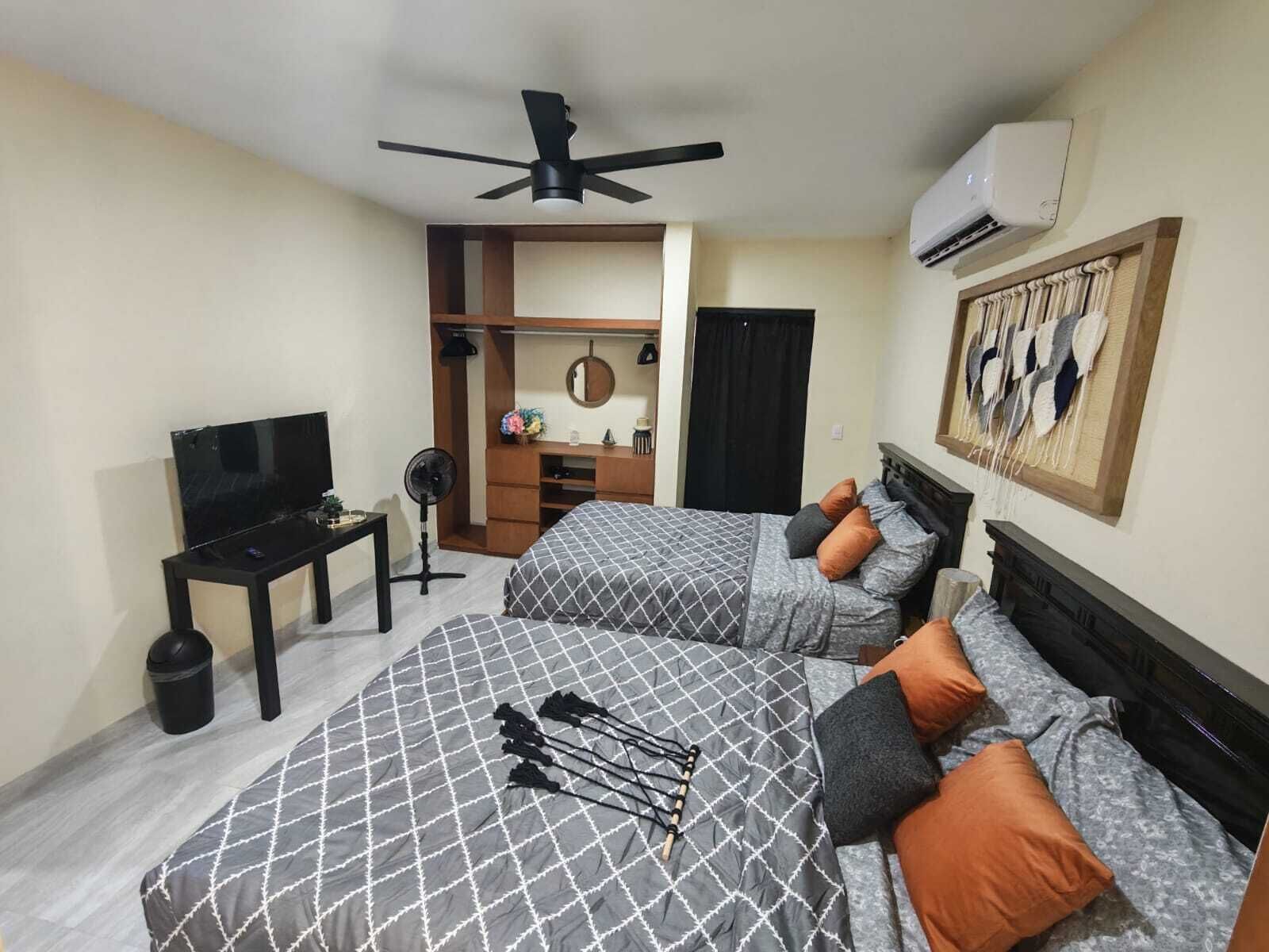 Une chambre d’hôtel avec deux lits, une télévision, un bureau, un ventilateur et un appareil de climatisation.