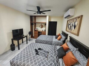 A hotel room with two beds, a TV, a desk, a fan, and an air conditioning unit. - Campo Cielo de Tita    2-bedroom apartment with AC in North Mérida (Mérida)