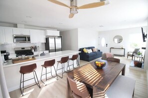 A modern kitchen with white cabinets, a stainless steel refrigerator, and a central island with bar stools. - Greater North Park Home + Fenced Yard (San Diego)